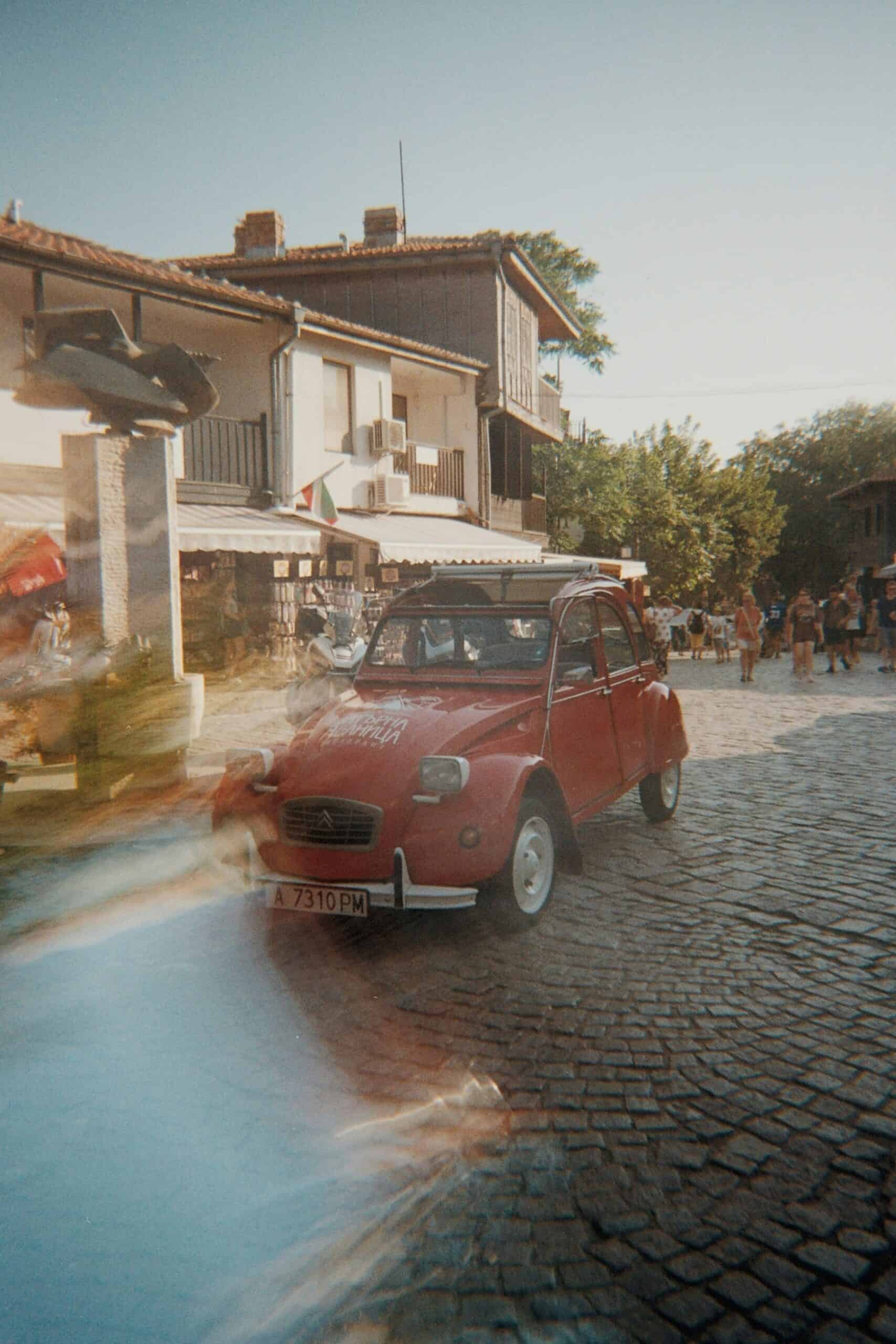 Vintage red microcar on cobblestone street in a charming town.